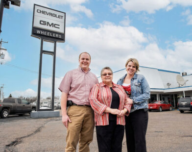 Mary Ann Wheeler standing in front of Dealership with her childern, Daniel and Mary Jo
