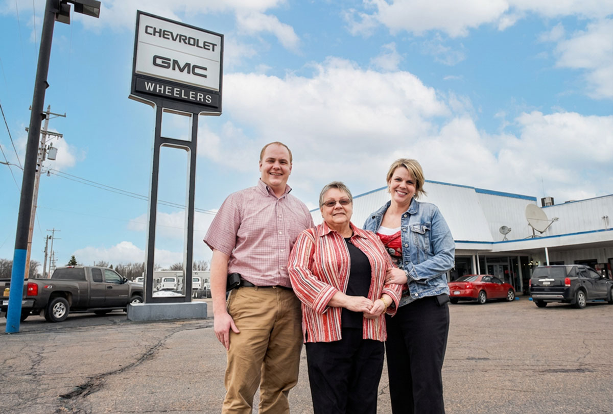 Mary Ann Wheeler standing in front of Dealership with her childern, Daniel and Mary Jo